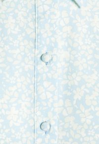 Camisa de manga curta azul claro com um padrão floral branco, fecho de botão e um tecido texturizado.