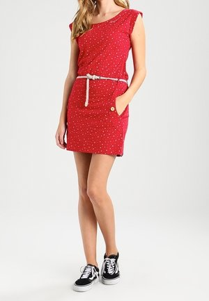 Rode jurk met korte mouwen, witte riem, bloemenpatronen en een zak. Gecombineerd met zwarte sneakers, met witte accenten en veters.