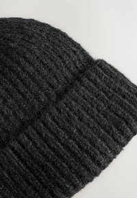 Black knitted beanie made of textured wool, featuring a ribbed pattern and a folded cuff, showcasing a soft, fuzzy appearance.