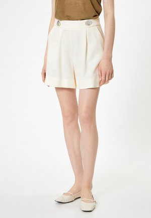 Crème-kleurige linnen shorts met plooien, hoge taille en twee decoratieve knopen. Soepele textuur en op maat gesneden pasvorm.