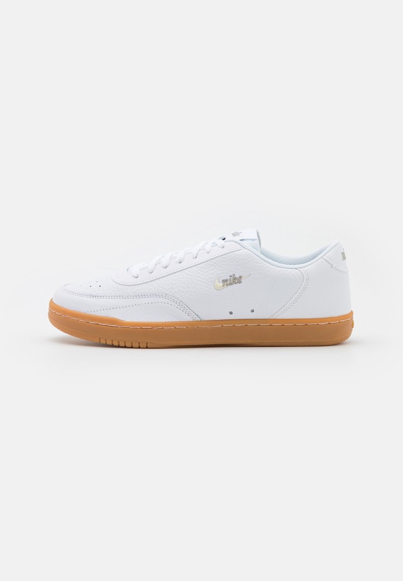 Baskets basses blanches Nike avec semelle en gomme et lacets blancs, vues de côté sur un fond clair uni.