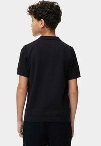 Camisa polo negra de manga corta con un patrón de punto texturizado en los hombros y un dobladillo acanalado, vista desde la parte posterior.