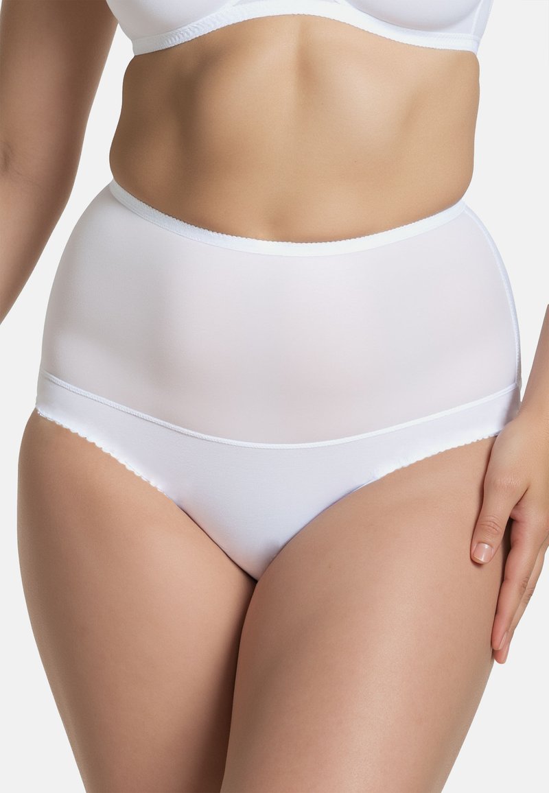 Vrouw in witte hooggeprijsde shapewear en bijpassende beha, met een gladde buik en heupen en één hand rustend op haar dij.