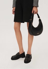 Czarne skórzane loafersy z masywnymi podeszwami i gładką fakturą. Do tego czarna skórzana torebka z złotym logo i zaokrąglonym designem.