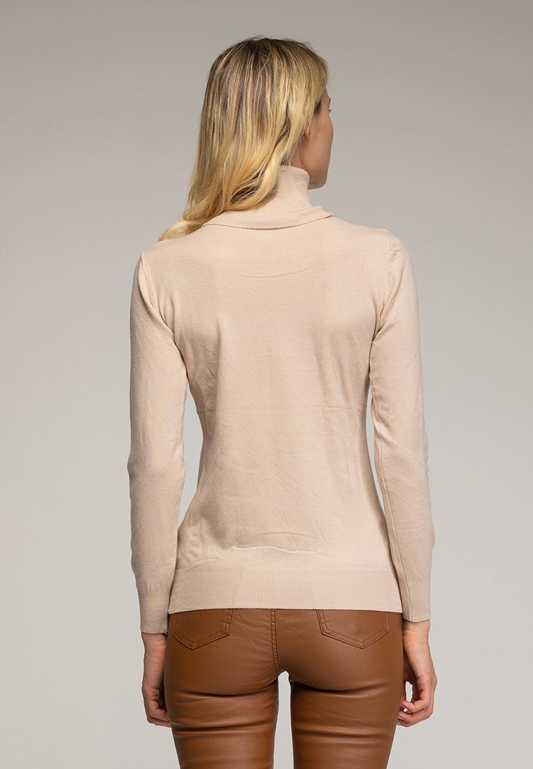 Beżowy sweter typu golf z prążkowanym wzorem, dopasowany krój i długie rękawy; zestawiony z brązowymi dopasowanymi spodniami. Widok z tyłu.