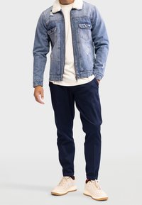 Kurtka dżinsowa z białym kołnierzem ze sztucznego baranka, dwoma kieszeniami na piersi i przetartymi elementami. Połączona z granatowymi zwężanymi spodniami i beżowymi trampkami.