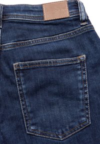 Mörka jeans med skräddarsydd passform, framträdande bakficka med gula sömmar och en ljusbrun läderetikett på midjan.