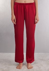Rode satijnen pyjamabroek met een elastische tailleband, rechte pijpen en een gladde textuur. Geleefde zoompjes voegen een afwerkingsdetail toe.