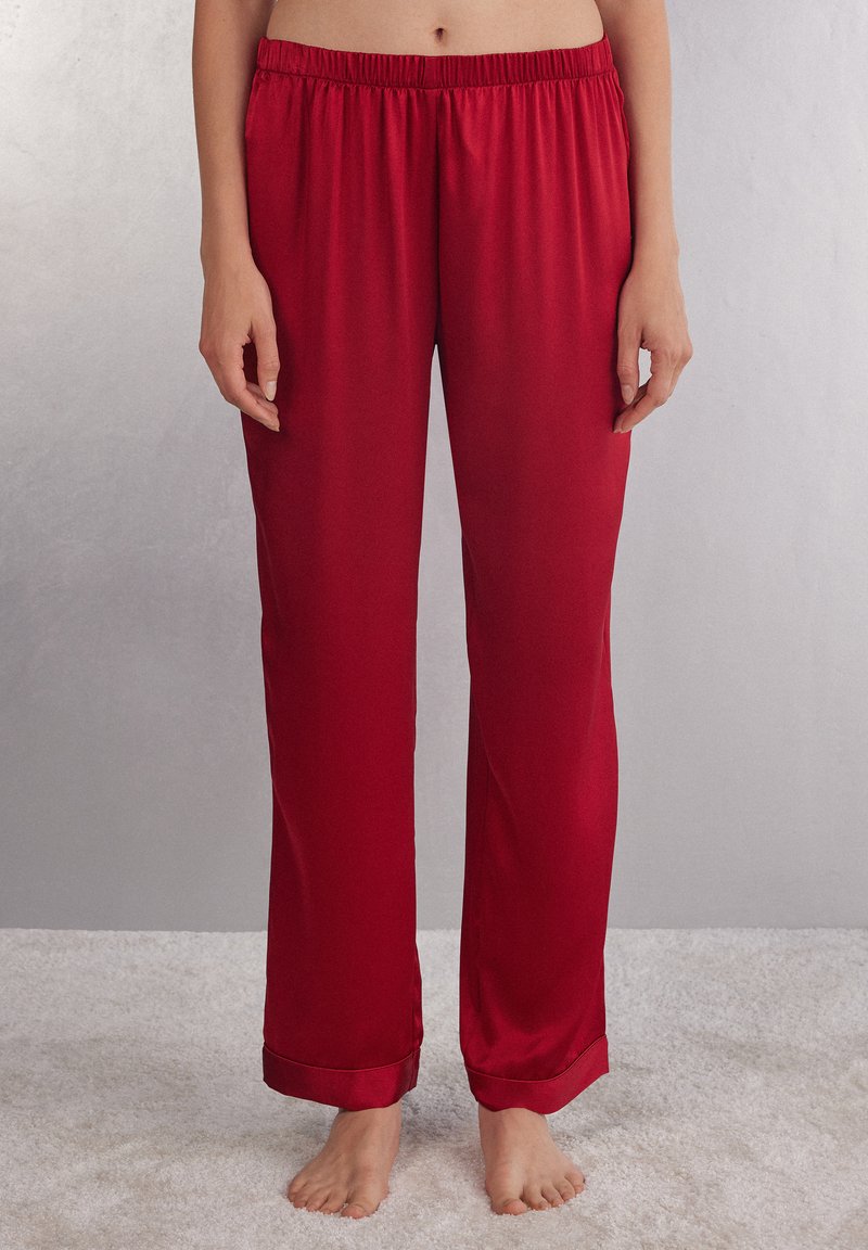 Rode satijnen pyjamabroek met een elastische tailleband, rechte pijpen en een gladde textuur. Geleefde zoompjes voegen een afwerkingsdetail toe.