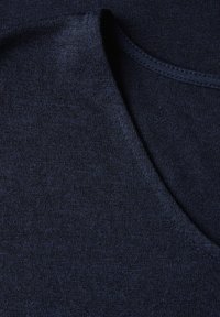 Námořnický modrý látkový materiál s hladkou texturou, vykazující kulatý výstřih a jemnou variaci v pleteném vzoru. Detailní záběr zvýrazňuje detaily.