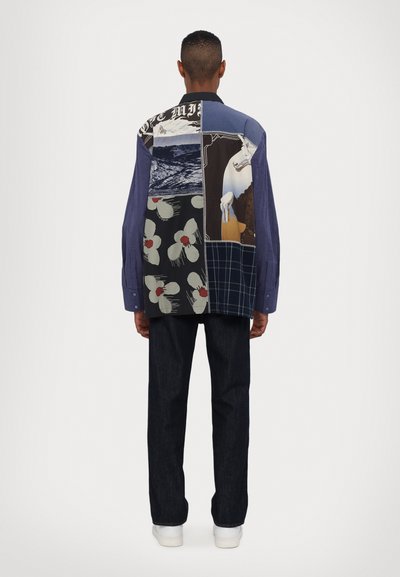 Multicolor, patchwork shirt with varied textures and patterns, featuring floral, graphic, and plaid designs. Complemented by dark denim pants.