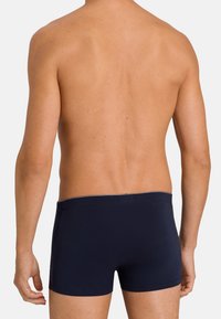 Námorně modré boxerky vyrobené z hladké tkaniny, s elastickým pasem. Pohled zezadu, který zvýrazňuje přiléhavý design.