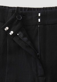 Pantaloni neri in tessuto con pattina zip, chiusure a bottone e due dettagli metallici, realizzati in materiale di lino testurizzato e con vita elastica.