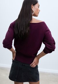 Pull en maille bordeaux avec un large décolleté et des manches amples, associé à une mini jupe en denim noir avec des poches arrière et un ourlet incurvé.