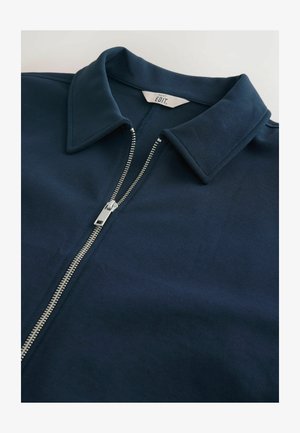 Navy blue zip-up jacket with a pointed collar, made of soft fabric, featuring a silver zipper running down the center. Clean design.