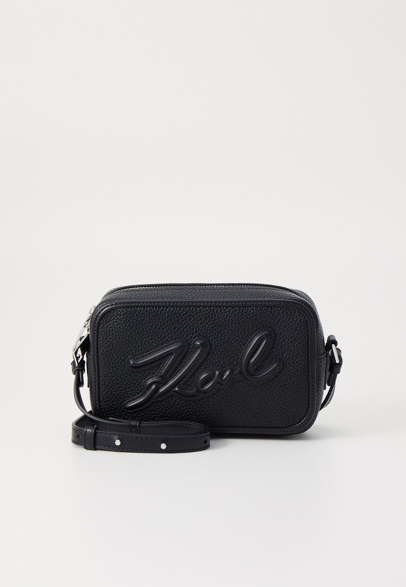 Bolsa crossbody de couro preto com uma superfície texturizada, logotipo em relevo "Karl", formato retangular e alça ajustável. Fecho de zíper na parte superior.