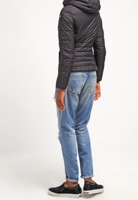 Svart vadderad jacka med huva, ribbad textur och tryckknappdetaljer; kombinerad med ljusblå slitna jeans och svarta slip-on skor.