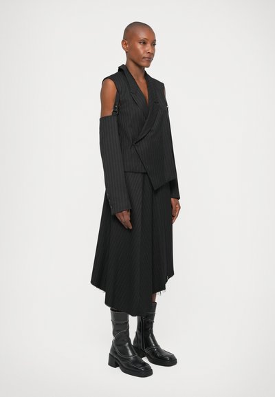 Melns svītrains žakete ar atvērtām piedurknēm, kombinēts ar atbilstošu asimetrisku svārku. Valkāts ar melniem ceļgalu garuma zābakiem. Gluda auduma tekstūra.