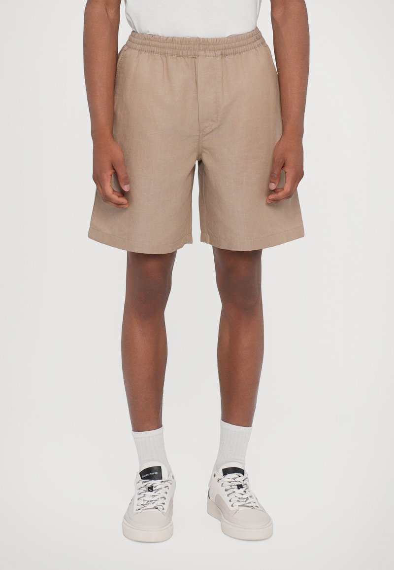 Khakifärgade shorts med elastisk midja, rak passform och sidofickor. I kombination med vita strumpor och ljusa sneakers.