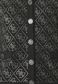 Black ribbed cardigan adorned with sparkling rhinestones in diamond patterns, featuring round metal buttons and two front pockets.