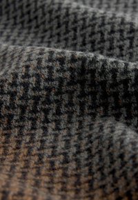 Woolen fabric with a houndstooth pattern in grey and black, featuring a soft, textured surface and subtle brown accents.