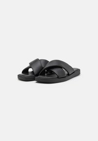 Schwarze Leder-Sandalen mit überkreuzten Riemen, flachen Sohlen und einer glatten Textur. Sie verfügen über ein minimalistisches Design ohne sichtbare Beschläge.