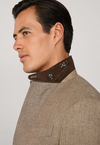 Beige Hahnentritt-Jacke mit einem braunen Lederkragen, der zwei Knöpfe und kontrastierende Nähte aufweist. Strukturierter Stoff mit passgenauer Passform.