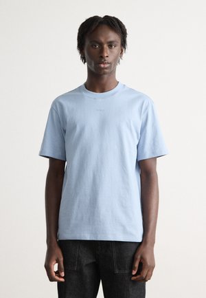 T-shirt en coton bleu clair à manches courtes et col rond. Présente un logo brodé subtil sur la poitrine. Stylisé avec un jean foncé.
