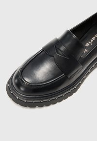 Melni ādas loafers ar noapaļotu purngalu, ar dekoratīvu siksnu un kniedētu gumijas zoli. Gluda tekstūra ar minimālām detaļām.