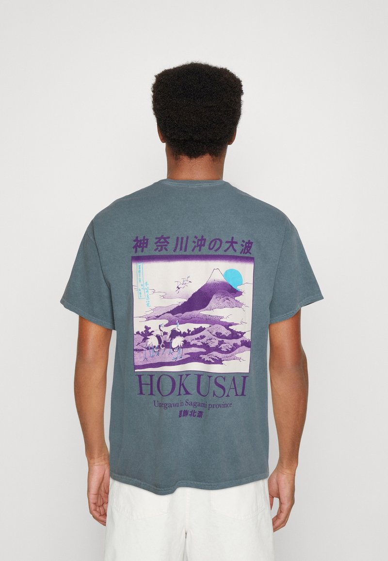 Grau-blaues Baumwoll-T-Shirt mit einem großen, bunten Hokusai-Druck auf dem Rücken, der einen Berg, Kraniche und stilisierte Wolken darstellt.