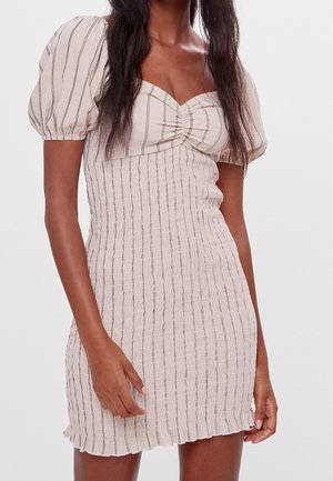 Woman wearing a short, beige, vertically striped dress with puffed sleeves and a ruched bust detail against a plain background.