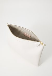 Pochette en cuir blanc avec un extérieur texturé et une fermeture zippée dorée. L'intérieur est en tissu beige avec une étiquette de marque visible.