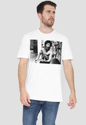 White t-shirt featuring a black and white photo print of a muscular person with an expressive face. Short sleeves, crew neck design.