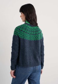 Sweter dziergany w ciemnym granacie z zielonym wzorem na karczku. Posiada ściągacze przy mankietach i dołem, fakturowaną tkaninę oraz luźny krój.