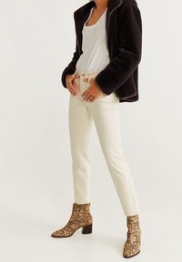 Veste en fausse fourrure noire, t-shirt blanc, jean crème ajusté et bottes à talons en cuir serpent marron à bout pointu.