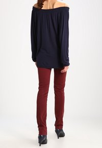 Granatowa bluzka na ramiączkach z długimi rękawami, sparowana z dopasowanymi burgundowymi spodniami i czarnymi szpilkami. Gładka faktura na całej powierzchni.