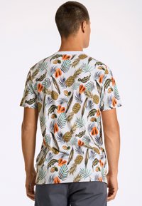 Kortärmad t-shirt med ett livligt tropiskt frukttryck i grönt, orange och gult på en vit bakgrund, i bomullsmaterial.