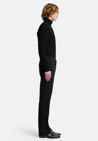 Maglione nero a collo alto, slim fit, abbinato a jeans neri. Tessuto liscio, design minimalista. Stivaletti neri alla caviglia completano il look.