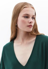 Grüner V-Ausschnitt-Pullover mit kurzen Ärmeln, aus einem weichen Stoff gefertigt, mit einem schlichten Design und glatter Textur.