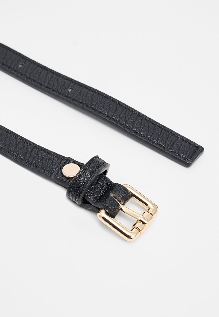 Schwarzer, texturierter Leder-Gürtelriemen mit einer glänzenden goldenen Metallschnalle und einem kleinen Druckknopf-Detail. Das Design ist elegant und minimalistisch.