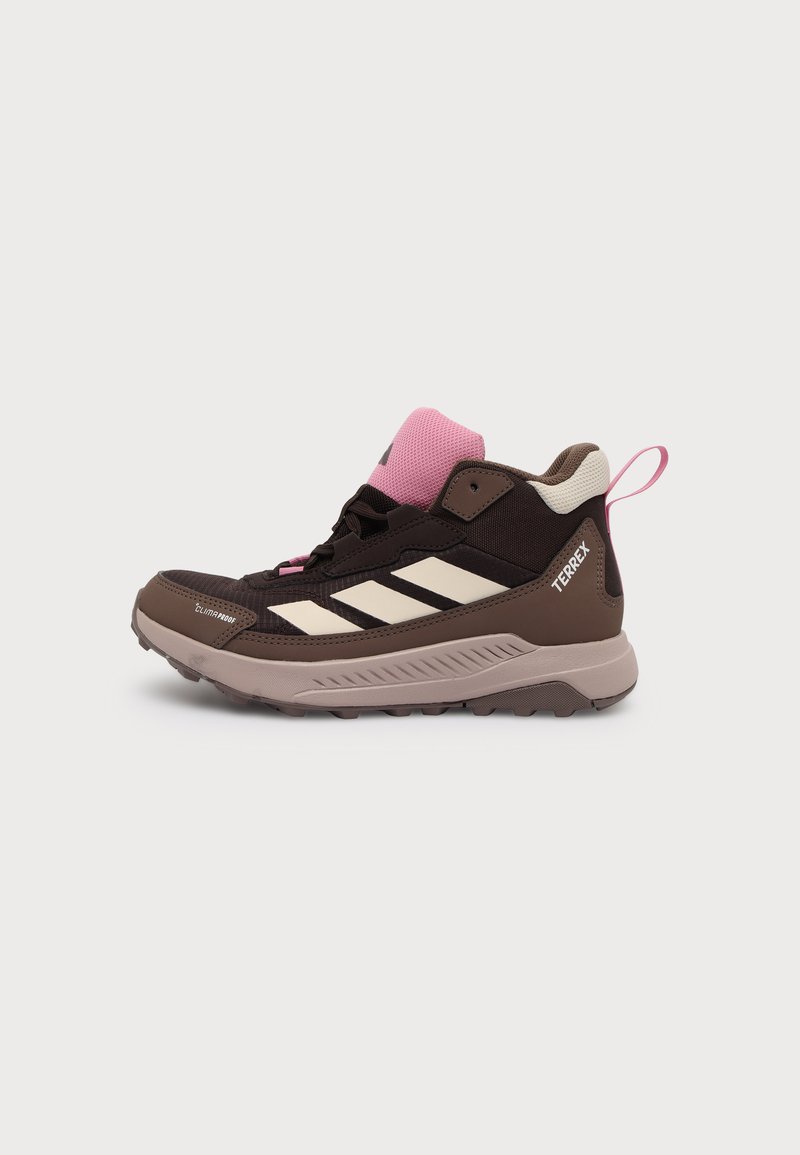 Καφέ και ροζ πεζοπορικό παπούτσι Adidas Terrex με μπεζ ρίγες, στιβαρή σόλα και τσάκιση σε ανοιχτό φόντο.