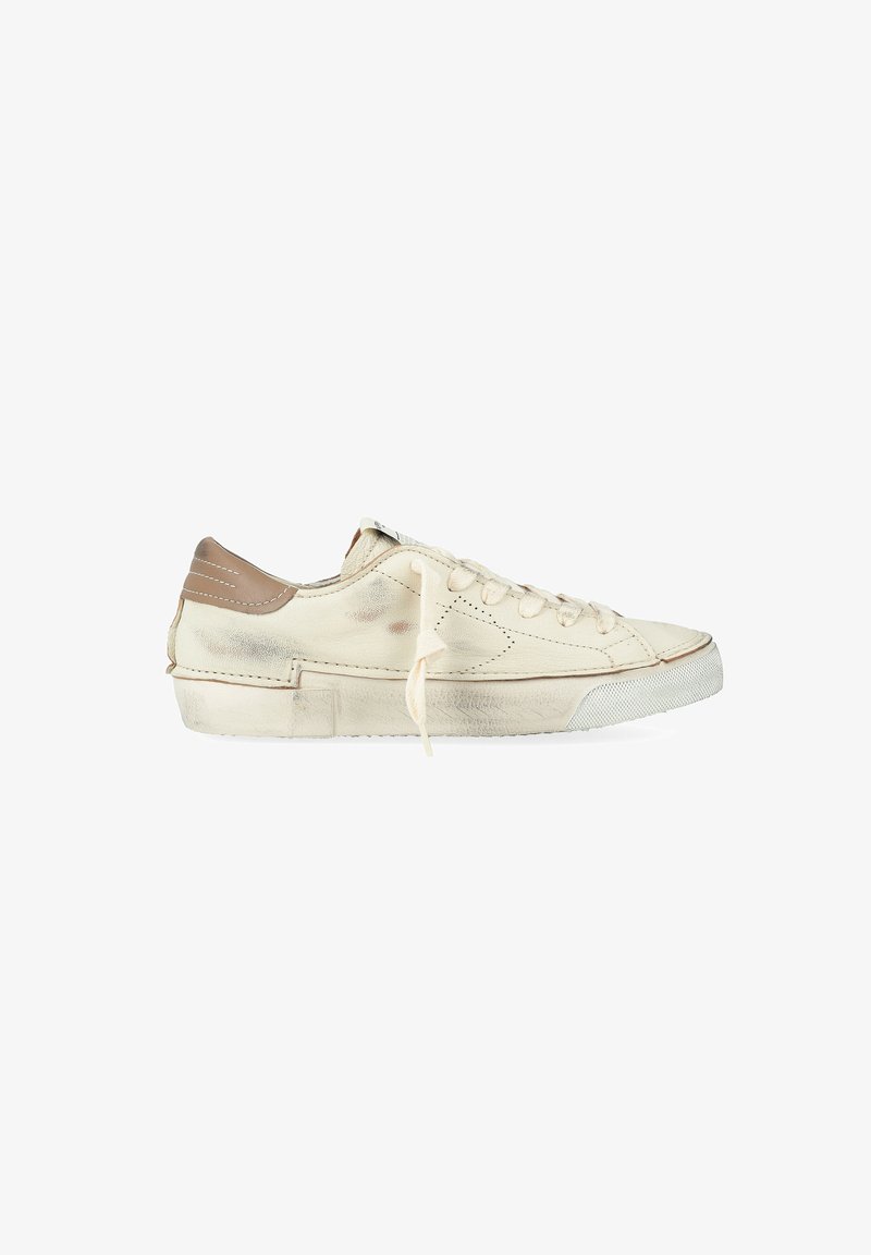 Sneaker low-top usata di colore bianco sporco con tallone beige, lacci bianchi e segni di usura visibili sulla suola e sul lato.