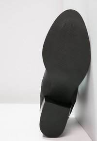 Stivale alla caviglia nero con una tomaia texture, un tacco rettangolare e una suola in gomma liscia. Presenta una punta leggermente arrotondata e strisce orizzontali sulla suola.