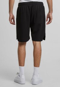Svarta texturerade shorts med elastisk midja och sidofickor. Har en enda bakficka, skär ovanför knäet, med en avslappnad passform.