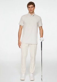 Polo de golf beige clair avec un col classique et des manches courtes, associé à un pantalon beige clair assorti et des baskets blanches.