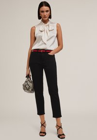Blusa blanca con un lazo en el cuello, pantalones negros ajustados, cinturón de cuero sintético rojo y sandalias negras con tiras. Lleva un bolso texturizado en blanco y negro.
