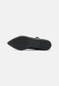 Zapato de tacón alto negro con punta afilada y suela de goma texturizada. Presenta acentos metálicos y un acabado elegante y suave.