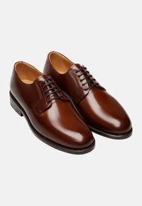 Braune Lederschuhe mit einer glänzenden Oberfläche, abgerundetem Zeh, Schnürdesign und dezenten Nähdetails im Obermaterial.