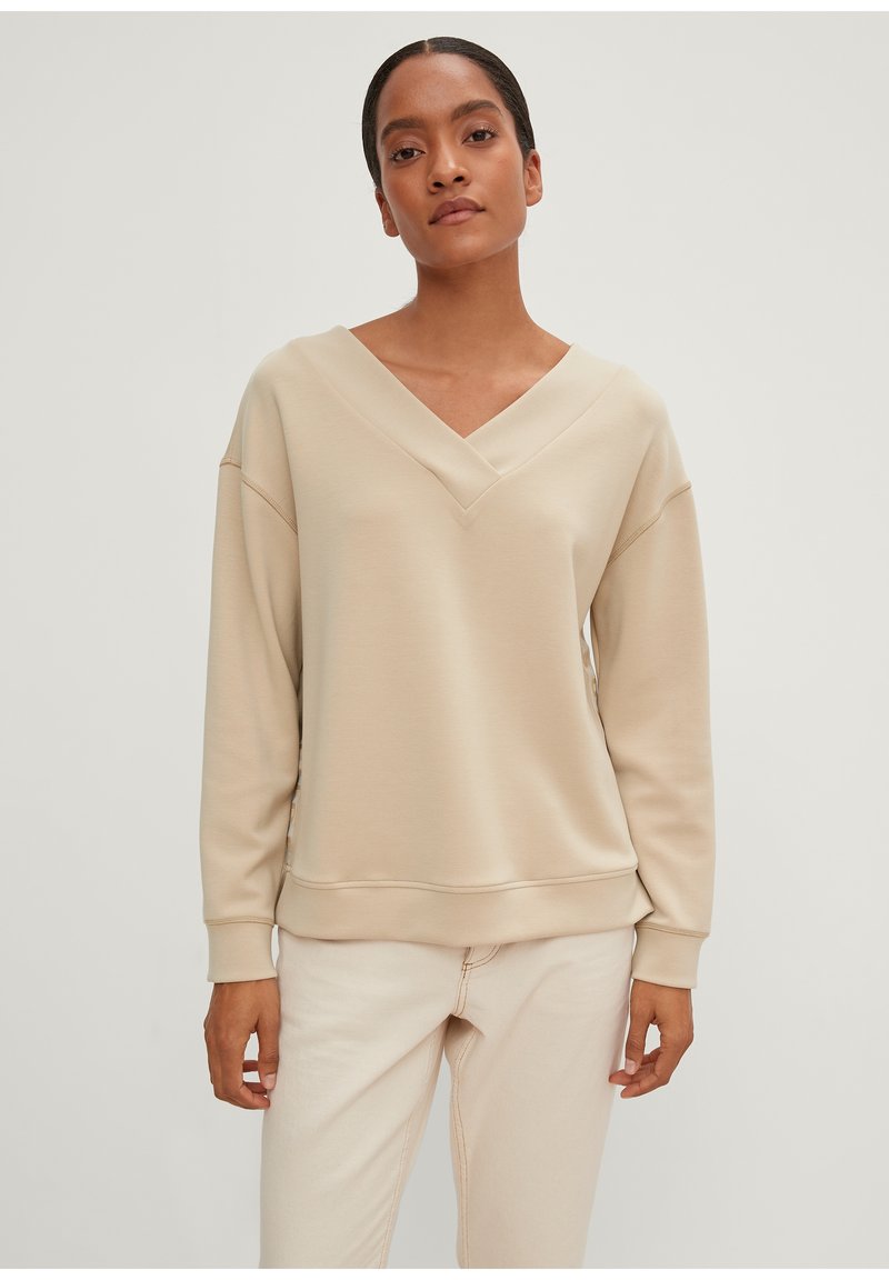 Beige sweatshirt med V-halsdesign og faldne skuldre. Fremstillet af blødt stof; har ribbede manchetter og kant. Bærer den med lyse jeans.