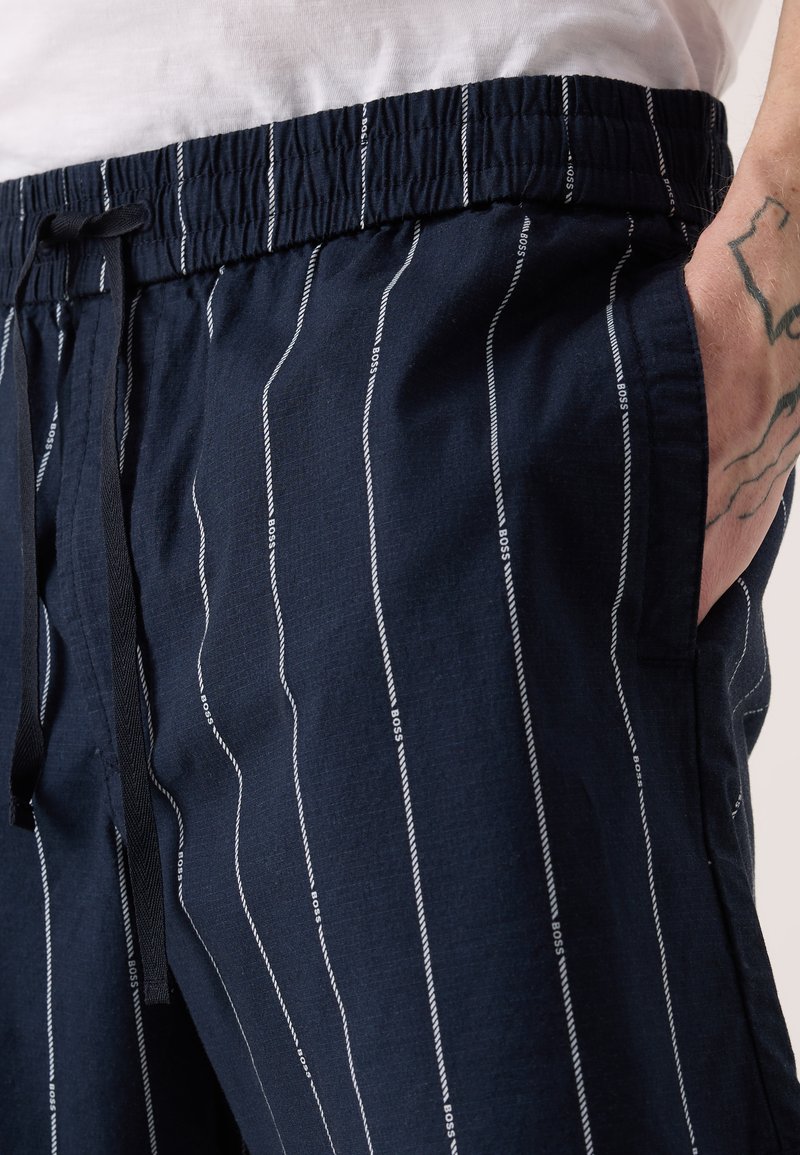 Marineblaue Lounge-Shorts mit weißen vertikalen Streifen, Kordelzugbund und seitlichen Taschen. Der Stoff hat ein weiches, strukturiertes Aussehen.
